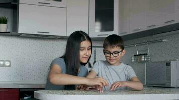 Beautiful boy and girl put together a puzzle while sitting at a table at home in the kitchen video