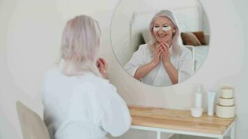 Skin Care, Senior Woman, Home Cosmetics, Elderly Age, Cosmetic Procedures. Serion woman uses eye patches while sitting in front of a mirror and smiling video