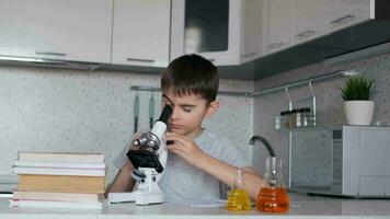 attraente ragazzo insegna biologia utilizzando un' microscopio e fa Appunti nel un' taccuino. compiti a casa. sinistra telecamera movimento video