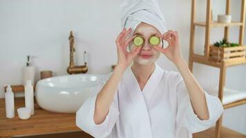 Skin Care, After Bath, Cosmetics at Home, Caucasian Woman, Anti Aging. Cheerful caucasian woman in a dressing gown and a towel on her head applies cucumbers to her eyes during cosmetic procedures video