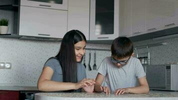 alegre lindo Garoto e menina vai enigma juntos enquanto sentado às uma mesa às casa dentro a cozinha video