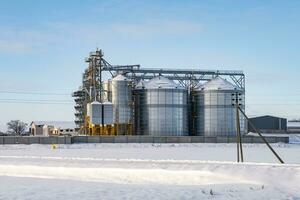 modern agro-processing plant for processing and silos for drying cleaning and storage of agricultural products, flour, cereals and grain in snow of winter field photo