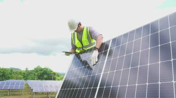 un joven ingeniero comprobación con un tableta el campo de fotovoltaica solar paneles operación solar paneles concepto renovable energía, tecnología, electricidad, servicio, verde, futuro. video