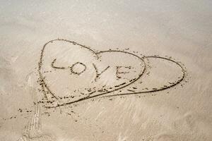 drawing in sand in form of two hearts and inscription love photo