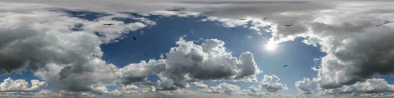 360 hdri panorama of blue overcast skydome with flock of birds in cumulus clouds, seamless sky panorama view with zenith for use in 3d graphics or game development or edit drone shot photo