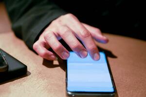 Hand of human play and touching his mobile phone on wooden table with bright lights of cafe. photo