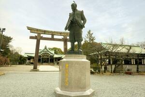 Osaka, Japan, June 20 2018 - Closeup Toyotomi Hideyoshi statue city ruler of Osaka city and Osaka castle in the Osaka castle park area and wooden torii gate with Japanese shrine on blue sky. photo