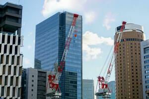 de cerca levantamiento grúas trabajando en ciudad paisaje ver y vaso oficina edificio con azul cielo y de seda nube antecedentes. foto