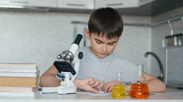 Attractive Boy teaches chemistry using a microscope and makes notes in a notebook. Homework. Left camera movement video