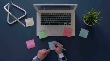 girl in a gray shirt sitting at the table thinks out and writes down on the stickers business ideas. overhead shot. 4k video