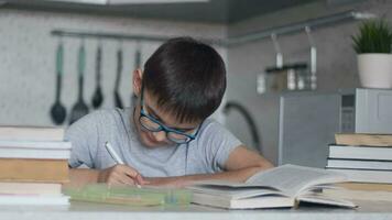 un' ragazzo con bicchieri fa compiti a casa utilizzando molti libri di testo e libri. telecamera mossa giusto video