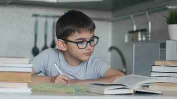 un chico con lentes lo hace deberes utilizando muchos libros de texto y libros. cámara movimiento video