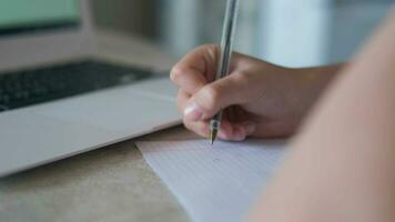 de cerca de manos con un fuente bolígrafo, ordenador portátil. un niño escribe en un cuaderno mientras haciendo deberes mientras sentado a un escritorio. video