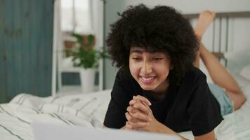 in linea apprendimento, africano americano alunno, distanza lezione, formazione scolastica a casa, seminario web conferenza. bellissimo afro americano donna utilizzando il computer portatile mentre fabbricazione in linea chiamata mentre dire bugie su letto video