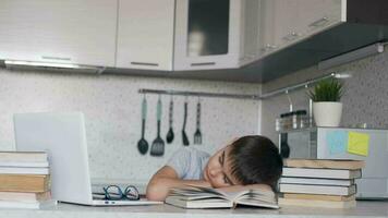 cansado colegial cayó dormido haciendo deberes sentado a un escritorio siguiente a un ordenador portátil y libros de texto moverse el cámara a el izquierda. distancia aprendizaje video