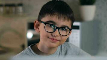 Stay at home, leisure at home, technologies for children, self isolation. A cheerful boy in glasses is watching cartoons while sitting at home using a laptop and eating popcorn. Look at the camera video