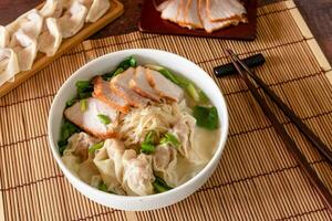 Closed up traditional Chinese food, wonton soup as stuffed dumpling with minced pork and slide roasted pork on wooden background photo