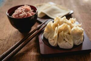 Closed up of raw Chinese dumpling and mince pork, ingredient for cooking on wooden table photo