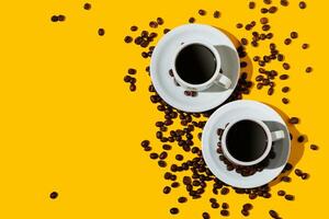 Top view of two coffee cup over a bright yellow color background and many beans spilled around. photo