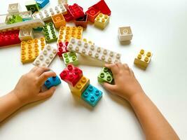 Child playing with colorful building blocks on white background. Top view photo