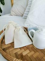 Cotton bags on a bamboo tray in a hotel room with a white bed photo