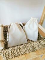 Wicker basket with white cotton bags on a wooden shelf against a white wall. photo