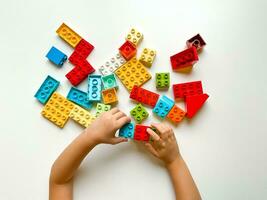 Child playing with colorful building blocks on a white background. Top view photo