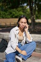 Portrait of sad girl talking on mobile phone and sulking. Young woman having an uneasy conversation on telephone, sitting on bench in park with upset face photo