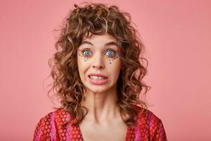 Close up photo of beautiful lady with big eyes opened feeling awkward, lifting eyebrows, saying oops, isolated over pink background