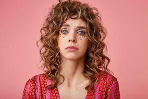 Portrait ot pretty blue-eyed curly young woman standing over the pink background, looking sad and unhappy, going to cry in despair photo