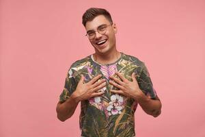 Indoor shot of handsome happy guy, looking at camera, looking joyful and happy, touching himsef with palms, isolated over pink background photo