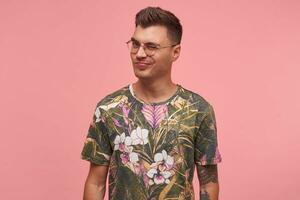 Portrait of handsome guy in t-shirt with floral print, looking at camera and giving a wink, being flirty and playful, posing over pink background photo