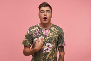 Portrait of attractive guy with dezad face, wearing glasses and flowered t-shirt, proving he is right, arguing, showing himself, isolate over pink background photo