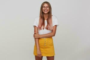 Studio shot of joyful young blonde female with casual hairstyle wearing white basic t-shirt and yellow skirt while posing over white background, being in high spirit and laughing cheerfully photo