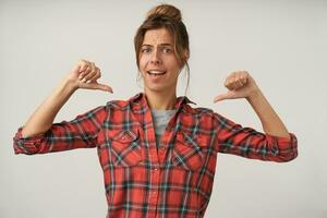 Indoor shot of attractive young self-confident woman with dark hair posing over white background in casual clothes, showing to herself with thumbs photo