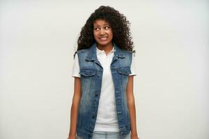Portrait of attractive young long haired brunette curly female with dark skin looking aside with oops face and showing her perfect white teeth, isolated over white background photo