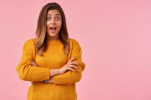 Joyful young lovely brown haired woman with casual hairstyle rounding amazedly her green eyes and keeping her mouth wide opened while looking at camera, isolated over pink background photo