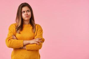 Bewildered young attractive brunette lady with natural makeup folding hands on her chest while posing over pink background, frowning eyebrows and pouting lips while looking confusedly aside photo