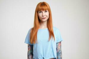 Studio photo of young lovely green-eyed redhead female with nose piercing looking positively at camera while standing over white background in casual wear