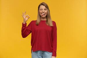 young woman, surprised girl with blond hair. Wearing red sweater and glasses. Pointing up with index finger on left hand like having a great idea. Looking camera isolated over yellow background photo