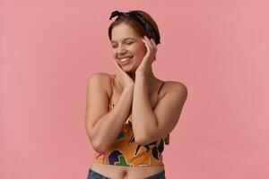 Image of european beautiful woman with natural makeup wearing trendy summer crop top slim strap and bandana with arms around face lovely shy emotion beautiful smile isolated posing against pink wall photo