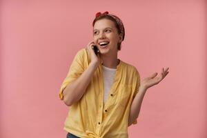 Portrait of beautiful european young woman wearing yellow shirt and red bandana with arms gesticulates on the phone smiling aside isolated posing over pink background emotion happy talking smiling photo