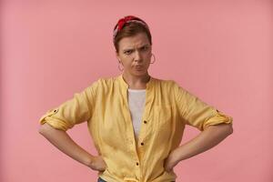 Portrait european brown haired woman 20s with natural makeup wearing stylish yellow shirt and red bandana posing against pink background emotion annoyed bored irritation looking at you hands on hips photo