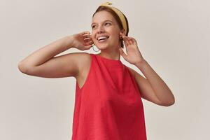 Portrait of attractive young brown eyed woman 20s wearing stylish trendy red dress and yellow bandana emotion happy glad smiling with fingers touching chicks look aside posing against white background photo