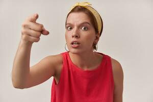 Image of european brown haired charming woman 20s with natural makeup wearing stylish trendy summer clothes and bandana pointing finger at you emotion judgment looking at you posing against white wall photo