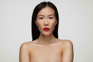 Closeup of pretty young brunette female with festive makeup keeping her red lips folded while looking seriously at camera, isolated over white background photo