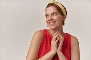 Image of european brown haired charming woman 20s emotion naughty cheerful flirting aside with natural makeup wearing stylish trendy red dress and yellow bandana posing against white background photo