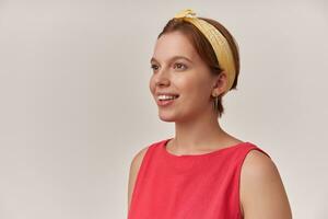 Portrait beautiful european young woman emotion happy glad smiling and looking aside nice face with natural makeup and earrings wearing stylish trendy red dress and yellow bandana against white wall photo