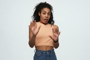 Shocked afraid african american keeps hands in front of herself and defending from threat young woman over white background photo