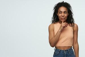 Smiling beautiful african american young woman showing silence sign and looking away to the side at empty space isolated over white background photo